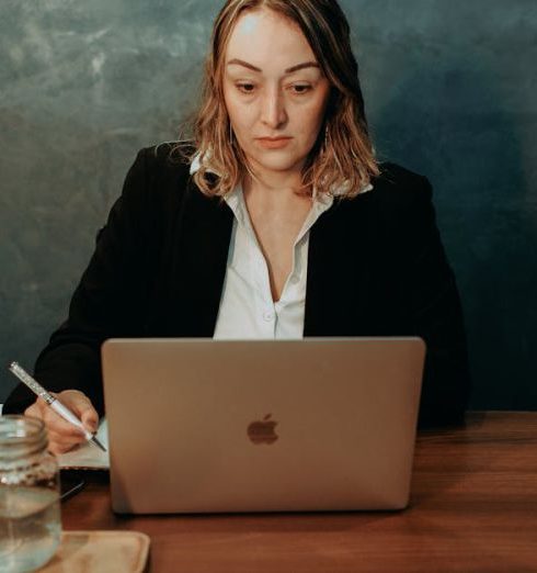 Employee Handbook - A focused businesswoman working on a laptop in a stylish office setting. Professional and determined demeanor.