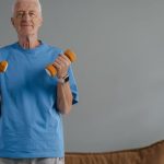 Wellness Programs - Elderly man lifting dumbbells indoors, promoting a healthy lifestyle.