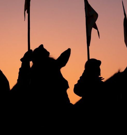 Disciplinary Actions - Dramatic silhouette of soldiers on horseback holding flags, against a colorful sunrise sky in New Delhi.