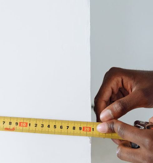 Metrics - Detailed shot of hands using a tape measure against a white wall indoors.