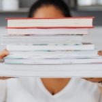 Learning Culture - Close-up of a person holding a stack of books indoors, showcasing academic focus.