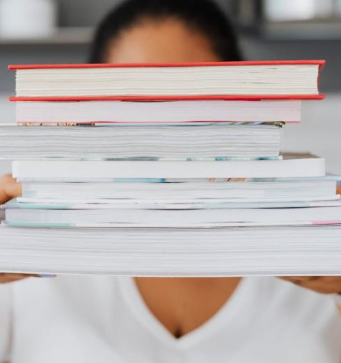 Learning Culture - Close-up of a person holding a stack of books indoors, showcasing academic focus.