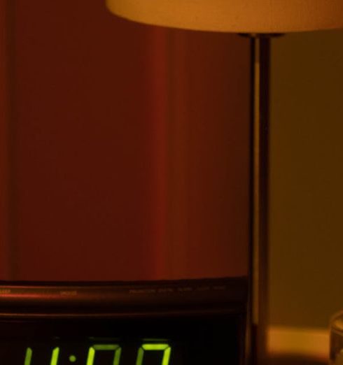 Paid Time Off - A warm and moody bedside table with a digital clock showing 4:08 and a lamp in dim lighting.