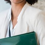 Career Development - Smiling woman in business attire holding a green file in an office setting.