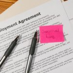 HR Policies - Top view of employment agreement contract with pens and seasonal hire note on wooden desk.