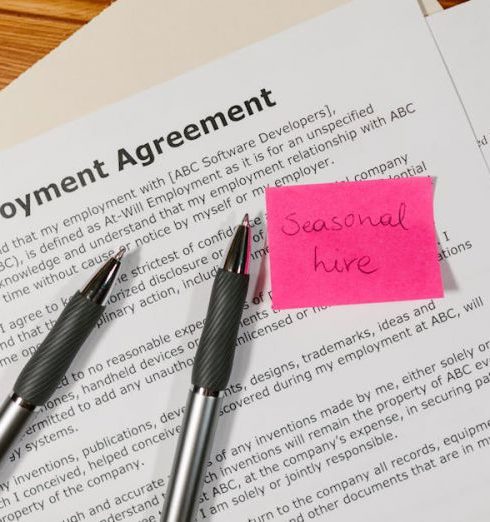 HR Policies - Top view of employment agreement contract with pens and seasonal hire note on wooden desk.