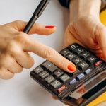 Metrics - Close-up of a woman using a calculator at her wooden workspace with documents and notepads.