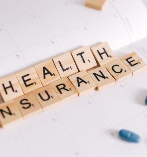 Long-Term Planning - Close-up of health insurance spelled out with Scrabble tiles on a planner, alongside medication pills.