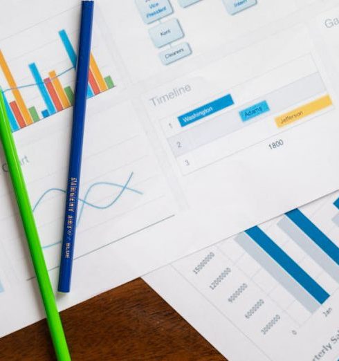 Benchmarking - Flat lay of various business charts and colored pencils on wooden table, highlighting financial analysis.