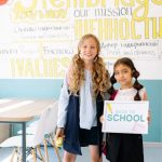 Mission Statement - Two young girls stand in a vibrant classroom, ready for back-to-school season.