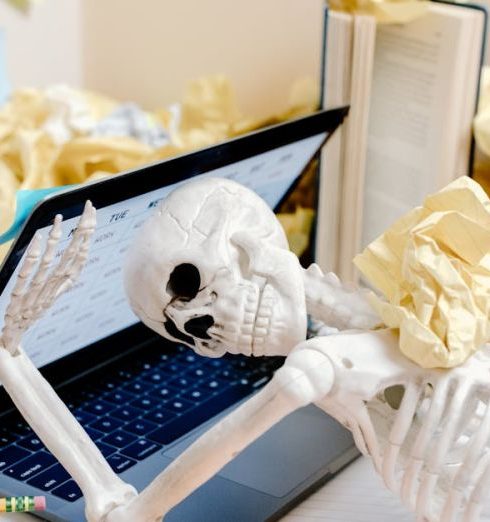 Deadlines - A skeleton surrounded by crumpled paper and books at a messy desk symbolizes burnout and overwork.