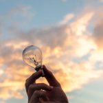 Innovation - A hand holds a light bulb against a scenic sunset sky, symbolizing creativity and innovation.