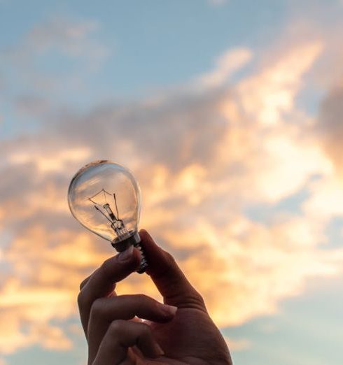 Innovation - A hand holds a light bulb against a scenic sunset sky, symbolizing creativity and innovation.