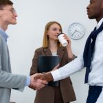 Employee Involvement - Three professionals in an office setting, shaking hands as a businesswoman observes.