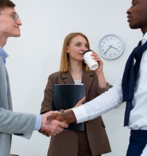 Employee Involvement - Three professionals in an office setting, shaking hands as a businesswoman observes.