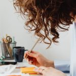 Strategic Budgeting - A woman in a blue blouse writing at a desk with a calculator and documents.