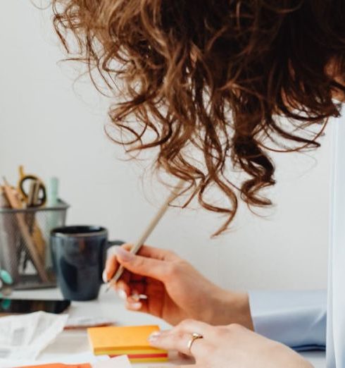 Strategic Budgeting - A woman in a blue blouse writing at a desk with a calculator and documents.