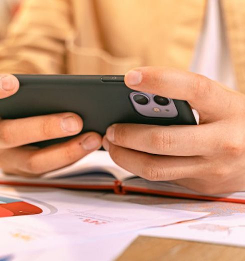 Strategy Updates - Woman Sitting at a Table and Using Smart Phone with an Open Notebook