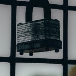 Risk Mitigation - Close-up image of a padlock hanging on a grating fence with a blurred outdoor background.