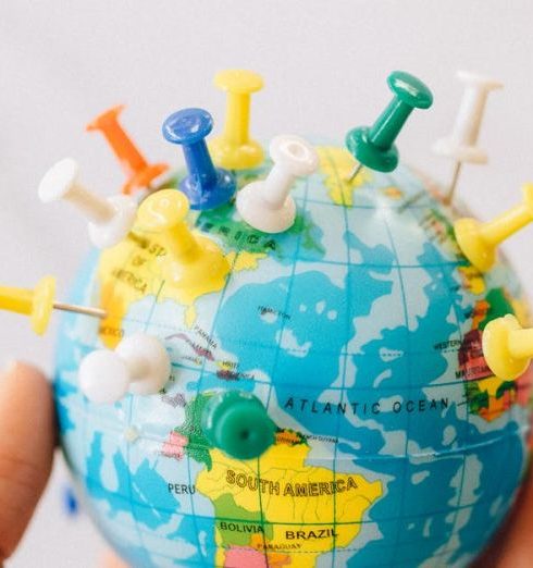 Continuity Planning - Close-up of a hand holding a mini globe with colorful push pins on a white background.