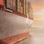 Supply Chain - A colossal cargo ship loaded with containers navigates through calm waters against a vibrant sunset sky.