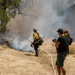 Environmental Risks - Firefighters in protective gear combating a spreading wildfire near a home.