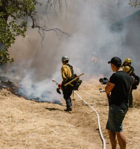 Environmental Risks - Firefighters in protective gear combating a spreading wildfire near a home.