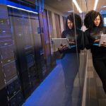 Data - A woman using a laptop navigating a contemporary data center with mirrored servers.