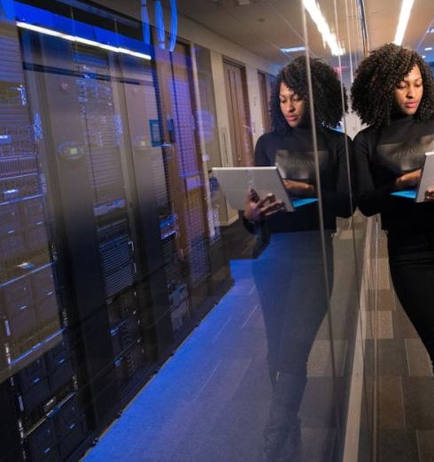 Data - A woman using a laptop navigating a contemporary data center with mirrored servers.