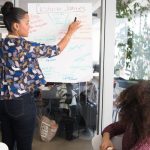 Business Strategy - Two women collaborating on project strategy using notes in modern office.