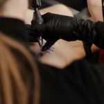 Regulatory Risks - A skilled tattoo artist focuses on creating a design on a client's shoulder in a modern tattoo studio.