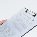 Compliance Management - Person holding a filled contract on a clipboard with a pen against a white background.