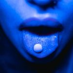 Risk Impact - Dramatic close-up of a person with a tablet on their tongue in blue lighting.