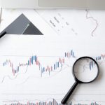 Predictive Analytics - Flat lay of stock market analysis documents with magnifying glass, pens, and glasses.