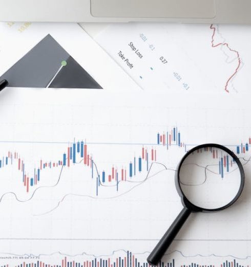 Predictive Analytics - Flat lay of stock market analysis documents with magnifying glass, pens, and glasses.