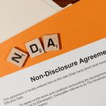 Intellectual Property - Top view of a Non-Disclosure Agreement with NDA in Scrabble tiles, emphasizing confidentiality.