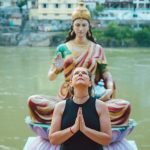 Awareness Culture - A woman praying beside a Hindu goddess statue by a river in Rishikesh, India.