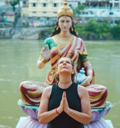 Awareness Culture - A woman praying beside a Hindu goddess statue by a river in Rishikesh, India.