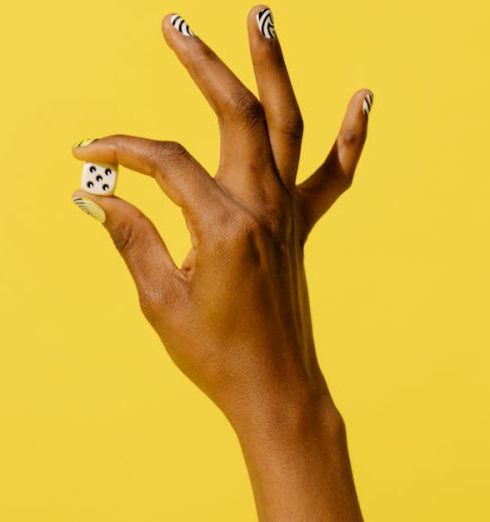 Emerging Risks - A hand with nail polish holds a dice, emerging from a hole against a yellow backdrop, creating a striking visual.