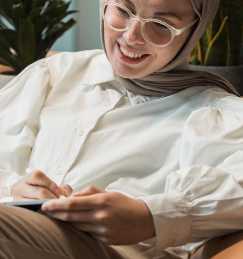 Corporate Culture - A smiling businesswoman wearing a headscarf relaxes on a sofa in a modern office lounge, surrounded by plants.