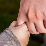 Trust - A close-up of a child and parent holding hands in a park, symbolizing love and trust.