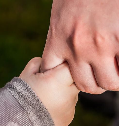 Trust - A close-up of a child and parent holding hands in a park, symbolizing love and trust.