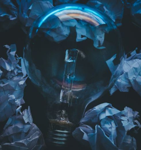 Innovation - A light bulb surrounded by crumpled paper symbolizes creative ideas and innovation in a dark setting.