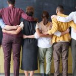 Diversity - A diverse group of adults in casual outfits hugging in front of a chalkboard, symbolizing teamwork.