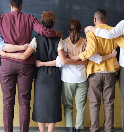 Diversity - A diverse group of adults in casual outfits hugging in front of a chalkboard, symbolizing teamwork.