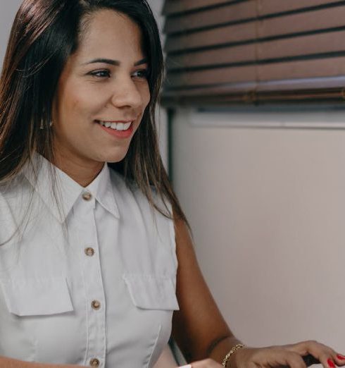 Employee-Centric - Professional woman in white shirt using computer at desk in modern office setting.