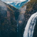 Turnover - Stunning aerial shot of a waterfall cascading down a rocky gorge with a bridge above in Norway's wilderness.