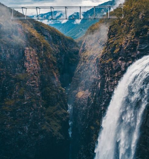 Turnover - Stunning aerial shot of a waterfall cascading down a rocky gorge with a bridge above in Norway's wilderness.