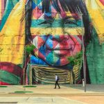 Culture - Colorful mural depicting a native face on an urban street wall with a passerby.