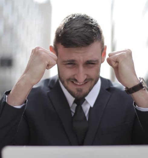 Purpose - A joyful businessman in a suit triumphantly celebrates success on his laptop outdoors.